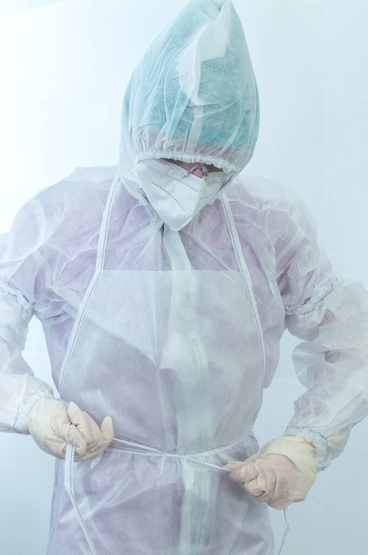 Der Prozess, einen medizinischen Schutzanzug gegen die Pest aus nächster Nähe anzuziehen. Junge Ärztin trägt medizinischen Schutzanzug im Kampf gegen Pandemie. - Foto, Bild