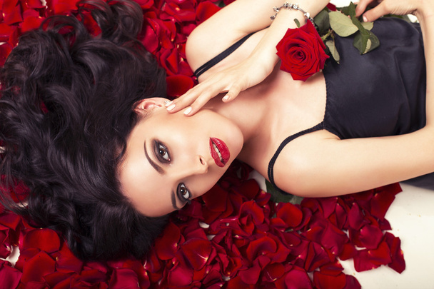 Beautiful woman with dark curly hair lying on carpet from rose's petals - Fotografie, Obrázek