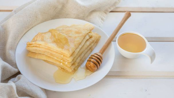 Pancakes  , honey and wooden honey spoon on a white plate . Pancakes on a white wooden table .   Russian blinis and honey top view .  - Photo, Image