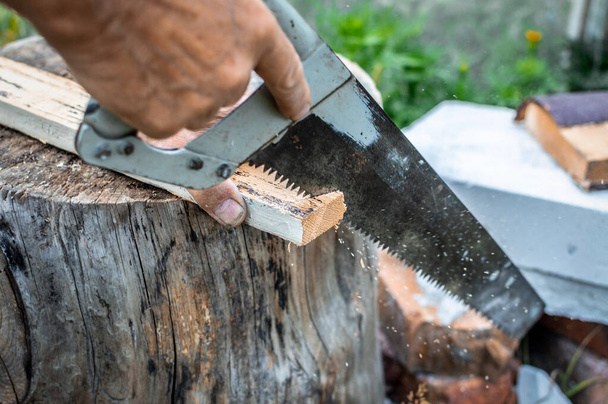 La mano de un hombre usa una sierra de mano para cortar un pedazo de una tabla de madera apoyada en un muñón. Carpintería exterior. - Foto, imagen
