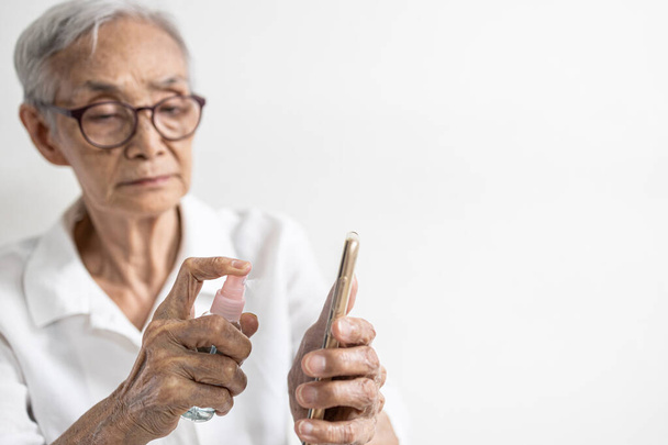 Ouderen die smartphones schoonmaken met behulp van alcohol-antiseptische spray, Aziatische senioren die alcohol spuiten, desinfecterende spray, tegen infectie van COVID-19-uitbraak, voorkomen besmetting met het Coronavirus - Foto, afbeelding