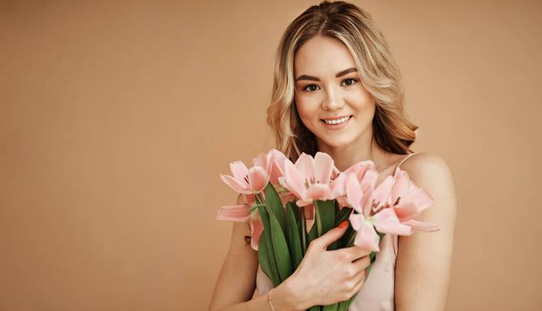Beautiful smiling woman on beige background with flowers - Foto, afbeelding