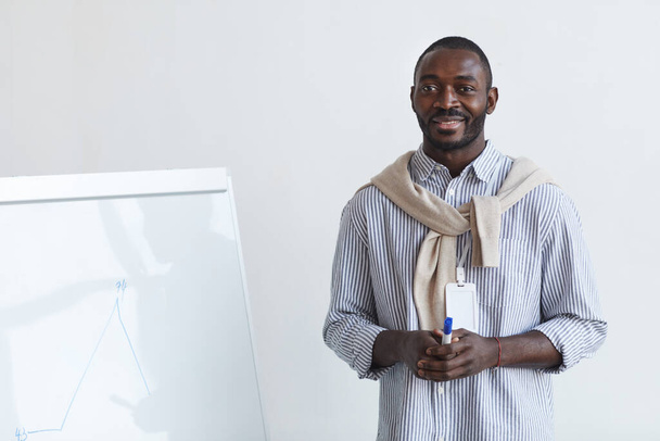 Porträt eines afroamerikanischen Businesscoaches, der auf Konferenzen oder Bildungsseminaren mit dem Publikum spricht, während er am Whiteboard steht und lächelt, Kopierraum - Foto, Bild