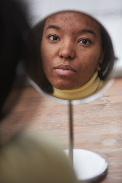 Gerçek Afrikalı Amerikalı bir kadının yansıması aynaya bakıyor cilt kusurlarına odaklanıyor, boşluğu kopyalıyor. - Fotoğraf, Görsel
