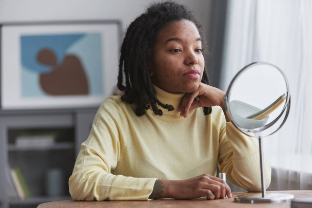 Portrét skutečné afroamerické ženy, jak se při pohledu do zrcadla namaluje, soustředí se na nedokonalosti pleti, kopíruje prostor - Fotografie, Obrázek