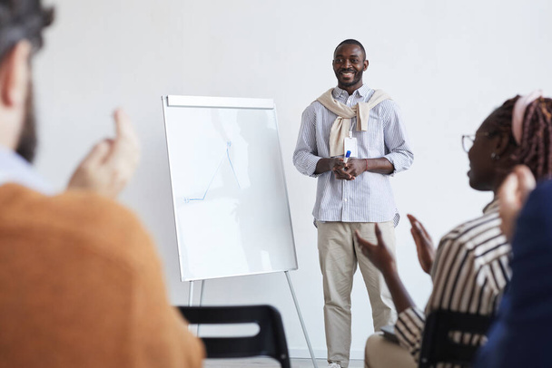 Plný portrét afroamerického obchodního trenéra mluvícího s publikem na konferenčním nebo vzdělávacím semináři, stojícího u tabule a usmívajícího se, kopírujícího prostor - Fotografie, Obrázek