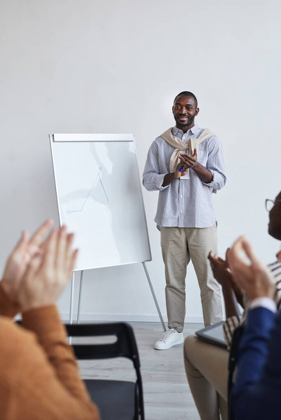 Вертикальний портрет афроамериканського бізнес-тренера, який розмовляє з аудиторією на конференції або освітньому семінарі, стоячи за білою дошкою і аплодуючи - Фото, зображення