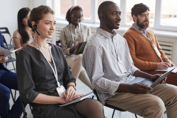 Grupo multiétnico de personas sentadas en sillas en la audiencia en la conferencia de negocios o seminario, se centran en la mujer joven con auriculares en primer plano - Foto, imagen