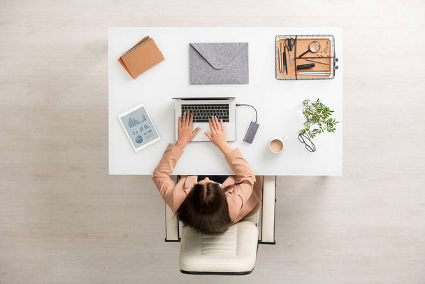 Áttekintés fiatal üzletasszony formalwear ül íróasztal előtt laptop és megérinti gombok, miközben adja meg az új adatok vagy hálózatépítés - Fotó, kép