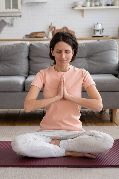 Жінка сидить у позі лотоса на йога килимок на підлозі вдома закриті очі, практикуючи вправи на йогу
. - Фото, зображення