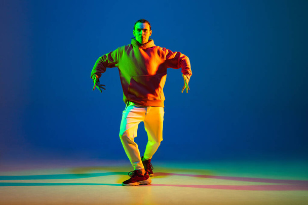 Молодая танцовщица хип-хопа танцует на голубом фоне в неоновом свете - Фото, изображение