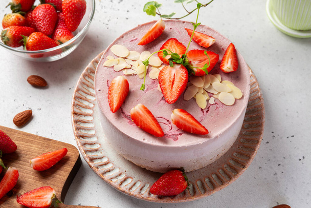 Close-up of raw vegan cake with almond and oatmeal flour, raisins and coconut butter base, cashew and strawberry mousse, gluten, egg and sugar free. Healthy food concept - Photo, Image