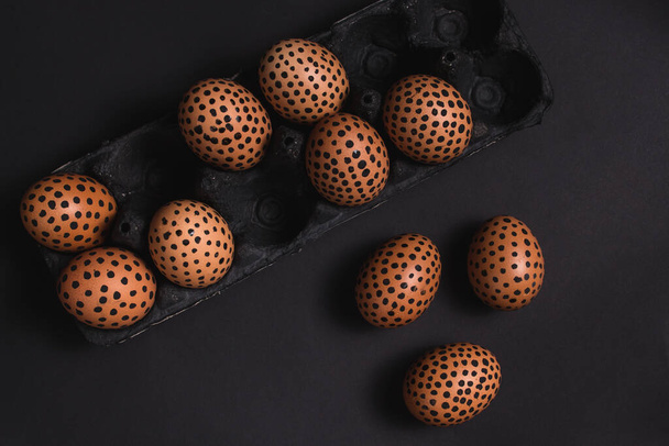 Painted easter eggs with black dots in an egg box. Top view of easter eggs on the black surface. Mockup for greeting, invitation cards and covers. Easter flat lay - Photo, Image