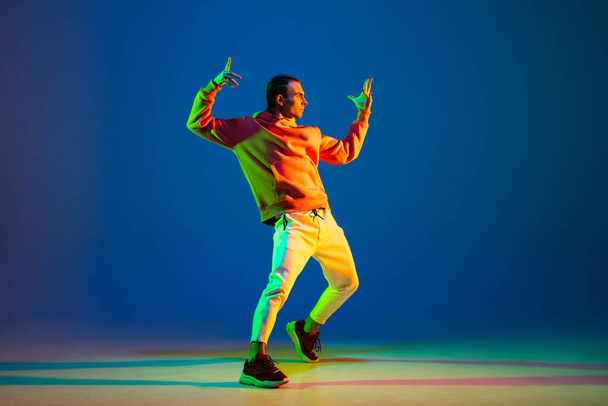 młody mężczyzna tancerz pozowanie izolowane na niebieskim tle w neon światło - Zdjęcie, obraz