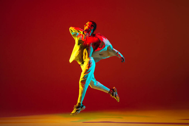 Fiatal fehér férfi táncol hip-hop elszigetelt piros háttér neon fény - Fotó, kép