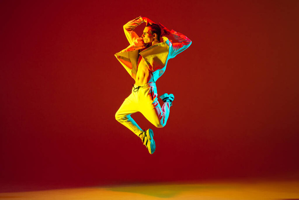 Jovem caucasiano dançando hip-hop isolado sobre fundo vermelho em luz de néon - Foto, Imagem