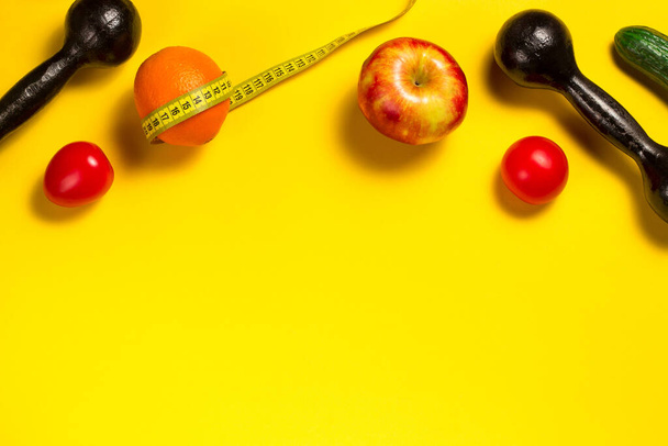 Creative flat lay of fitness equipment and fruits and vegetables on the yellow. Healthy lifestyle concept. Copy space. Orange with a tape measure, summer body concept. Trend color of the year 2021 - Photo, Image