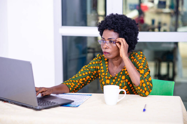 Mujer de negocios adulta seria sosteniendo gafas montura y trabajando en un ordenador portátil en la oficina. - Foto, Imagen