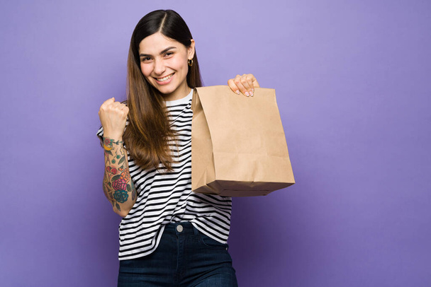 Izgatott fiatal nő boldog, hogy megkapja a kaját ebédre. Spanyol nő mosolyog, és kezében egy barna táska szállítási élelmiszer - Fotó, kép