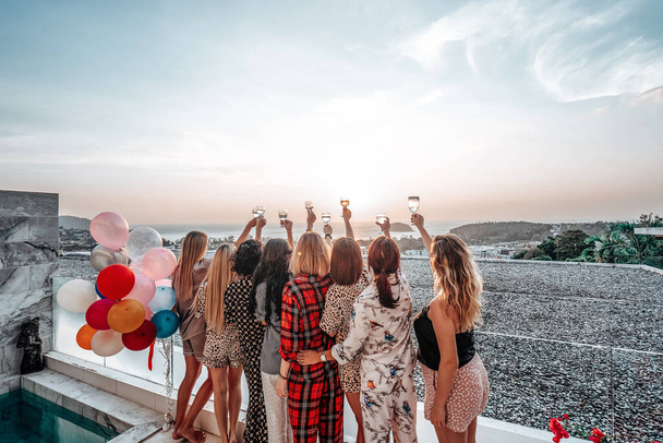 Eight female friends rise their hands up to sky holding champagne on rooftop - Photo, Image