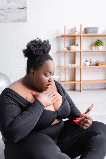 shocked african american plus size woman in sportswear looking at smartphone  - Photo, Image