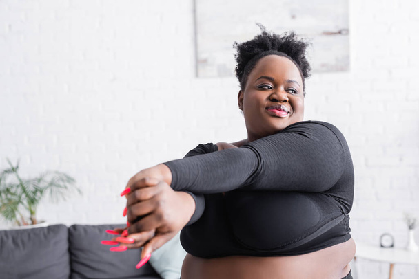 mujer afroamericana con sobrepeso en ropa deportiva haciendo ejercicio en casa - Foto, imagen