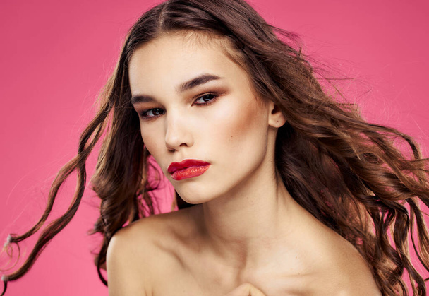 Rode lippen mooie brunette krullend haar roze achtergrond - Foto, afbeelding