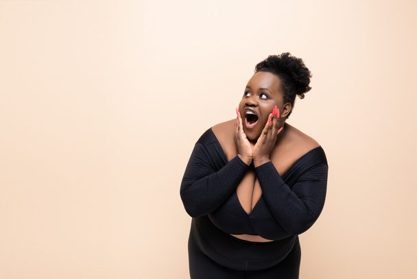 σοκαρισμένη Αφροαμερικανή συν μέγεθος γυναίκα κοιτάζει μακριά απομονωμένη σε μπεζ  - Φωτογραφία, εικόνα