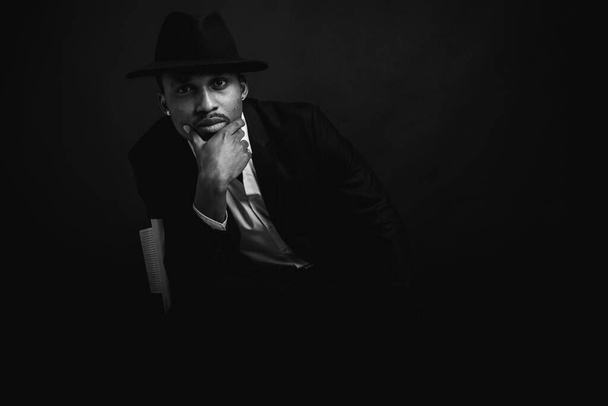 Portret atrakcyjnego, przystojnego, stylowego, profesjonalnego afro-amerykańskiego biznesmena w stylowym garniturze i białej koszuli, trzymającego się blisko twarzy, odizolowanego na ciemnym tle. Niski poziom. Ognisko selektywne - Zdjęcie, obraz
