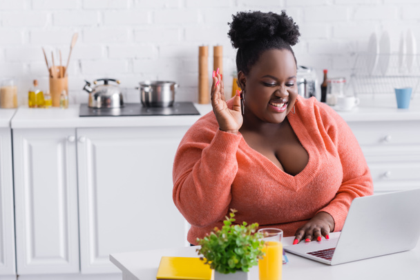 glückliche afrikanisch-amerikanische plus size Freelancer mit erhobener Hand mit Laptop zu Hause - Foto, Bild