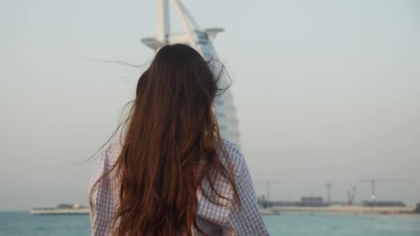 Nainen katselee Burj Al Arab hotellia Dubaissa auringonlaskun aikana. Takaisin näkymä naisten turisti tarkastella kuuluisa nähtävyys Dubaissa - Materiaali, video
