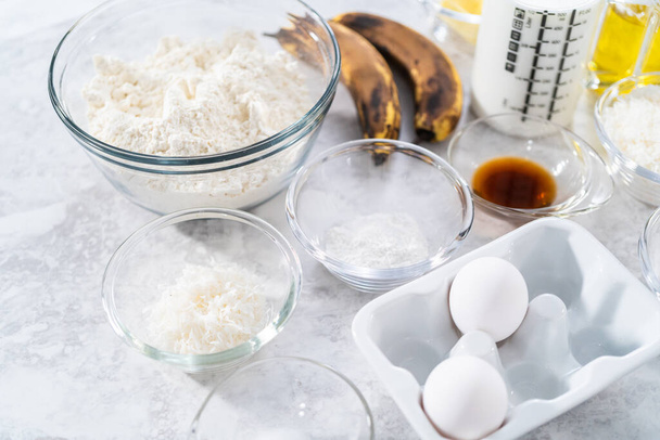Ingrédients mesurés dans des bols en verre pour préparer des crêpes à la banane à la noix de coco pour le petit déjeuner. - Photo, image