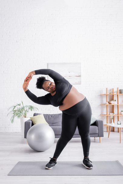 plná délka kudrnatý africký Američan plus velikost žena ve sportovním oblečení cvičení na fitness podložka - Fotografie, Obrázek