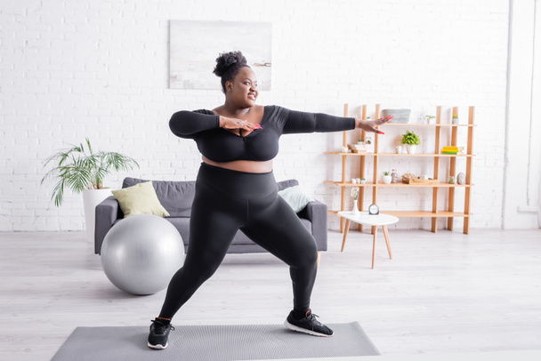 piena lunghezza di piacere africano americano plus size donna in abbigliamento sportivo esercizio in soggiorno - Foto, immagini