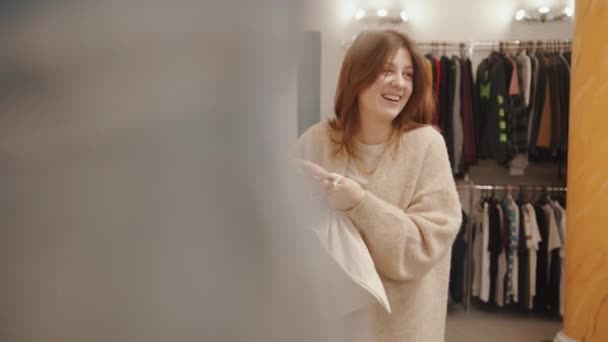 Stilvolles junges Mädchen kauft in einem Bekleidungsgeschäft ein und lacht, während sie mit jemandem spricht - Filmmaterial, Video