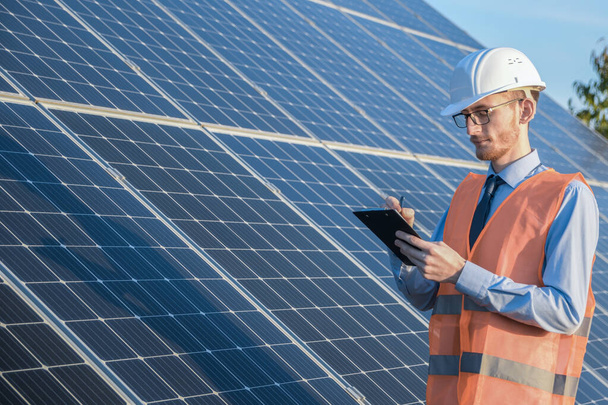 Engineer in uniform standing on a background of solar panels.The solar farm check the operation of the system, Alternative energy to conserve the world's energy, Photovoltaic module idea for clean energy production - Photo, Image