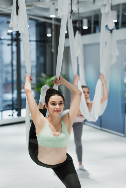 mujer sonriente estirándose con las hamacas aéreas del yoga en el gimnasio - Foto, imagen