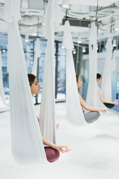 grupo de mujeres meditando en pose de loto mientras practican yoga con mosca, fondo borroso - Foto, Imagen