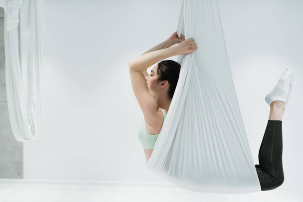 Vista lateral de la deportista haciendo ejercicio sobre mosca yoga hamaca en gimnasio  - Foto, imagen