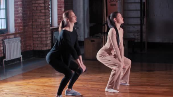 Deux femmes minces s'entraînent ensemble dans la salle de gym - accroupi avec un haltère - Séquence, vidéo