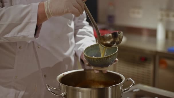 Detailní video rukou kuchaře v rukavicích na jedno použití, který nalévá tradiční japonskou polévku Ramen v modré keramické míse v kuchyni. - Záběry, video