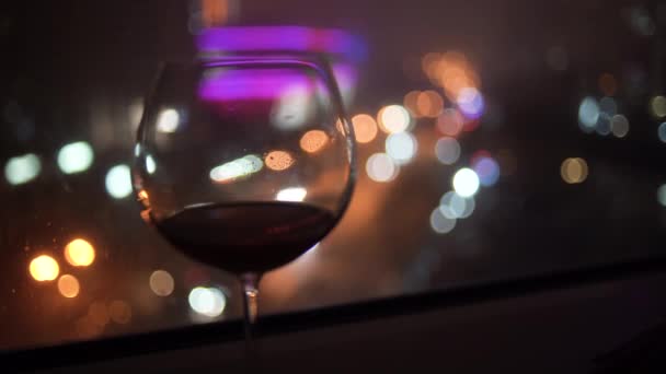 glas wijn op de achtergrond van de nachtstad, selectieve focus. Een vrouwenhand pakt een glas wijn op. Kopieerruimte. - Video