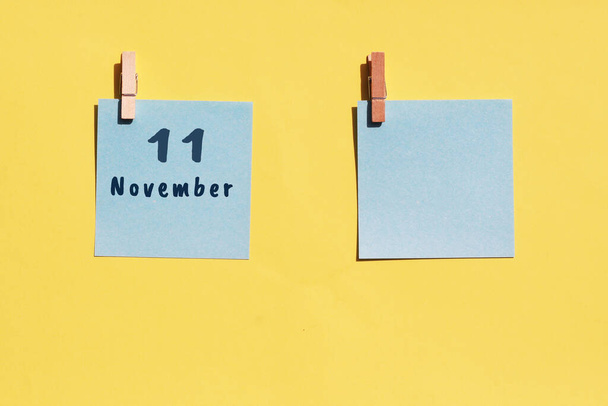 11 listopad. 11 dzień miesiąca, data kalendarzowa. Dwie niebieskie kartki do pisania na żółtym tle. Widok z góry, odbiór. Jesienny miesiąc, koncepcja dnia roku. - Zdjęcie, obraz