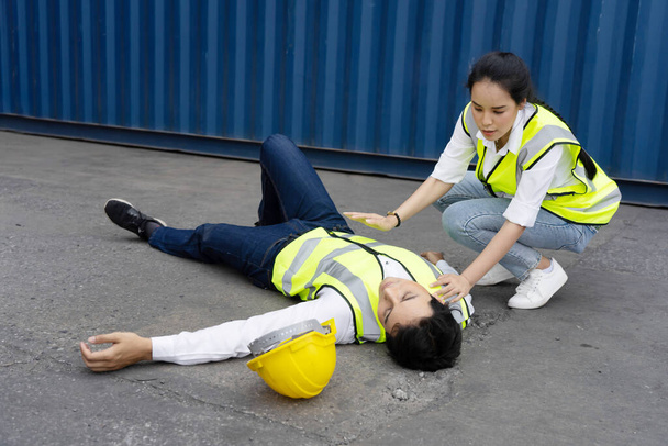 Asiatische Arbeiterinnen überprüfen ihre ohnmächtige Kollegin im Containerlager - Foto, Bild