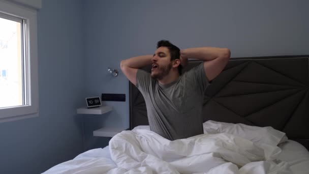 眠った後、若いラテン系の男性がベッドの中であくびとストレッチ。スローモーション。4kビデオ. - 映像、動画