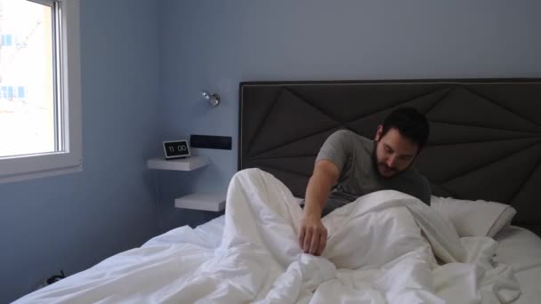Jonge Latijnse man geeuwt en strekt zich uit in bed na het slapen. 4k video. - Video