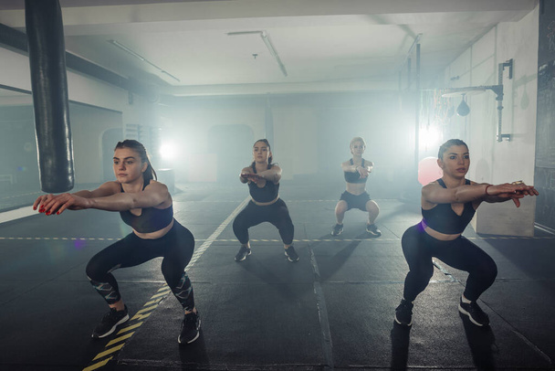 Four young female athletes are doing squats, wearing trendy sports outfit. - Foto, Imagem
