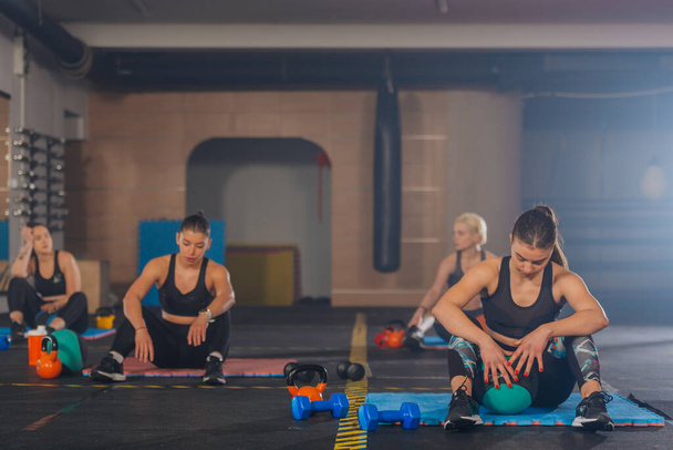 Attraktive Sportmädchen, die sich von Bauchmuskelübungen mit med ball im Gruppen-Fitnesstraining ausruhen - Foto, Bild