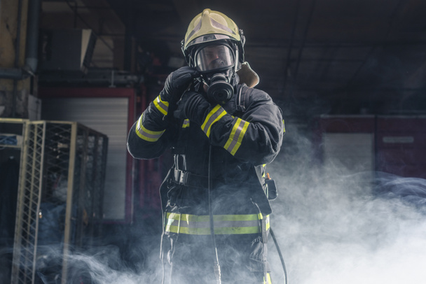 Портрет пожарного с явкой пожарного и шлемом. Темный фон с дымом и синим светом. - Фото, изображение