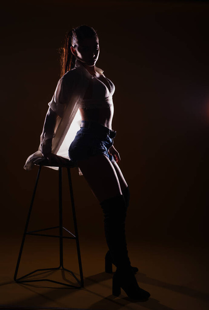 Полноразмерный силуэт на тёмном фоне сенсационной женщины, позирующей с высоким стулом - Фото, изображение